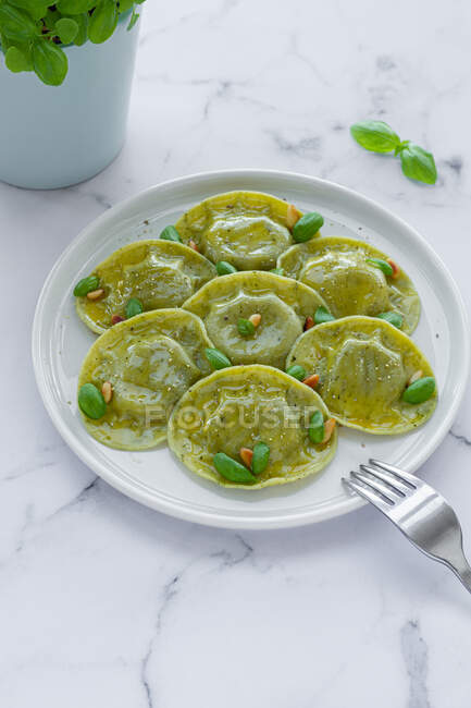 Top view of tasty raviolis with basil decorated with pine nuts served on white round plate on table in light kitchen — Stock Photo