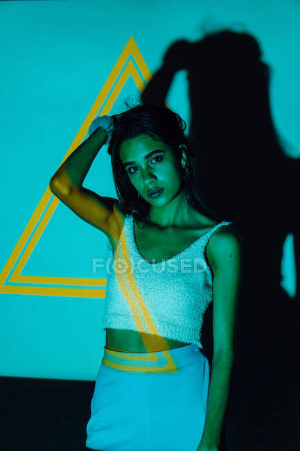 Cool young ethnic female in crop top looking at camera against yellow triangle and shadow — Stock Photo