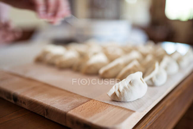 De arriba de las albóndigas de jiaozi tradicionales crudas servidas en la tabla de cortar de madera en la cocina - foto de stock