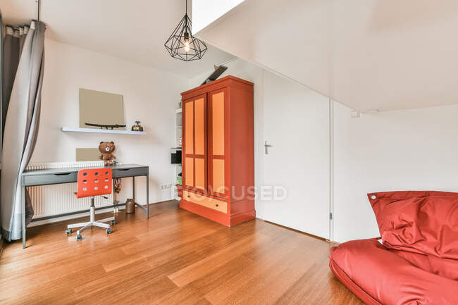 Sedia a tavolo con orsacchiotto posizionato vicino armadio colorato in luce camera moderna con borsa rossa sedia in appartamento — Foto stock