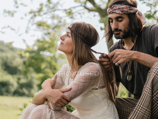 Attraktive Frau im durchsichtigen Kleid schaut weg, als ihr Freund ihr die Haare flechtet — Stockfoto