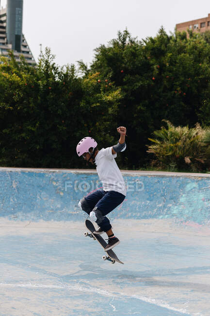 Ganzkörper junger ethnischer Mensch in lässigem Outfit mit Schutzhelm mit Knie- und Ellbogenpolstern beim Skateboardfahren im Skatepark — Stockfoto