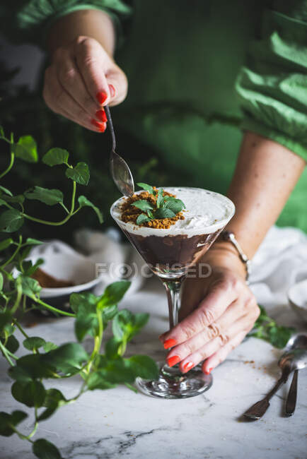 Unrecognizable female holding with spoon chocolate and coconut mousse on marble table with green plants — Stock Photo