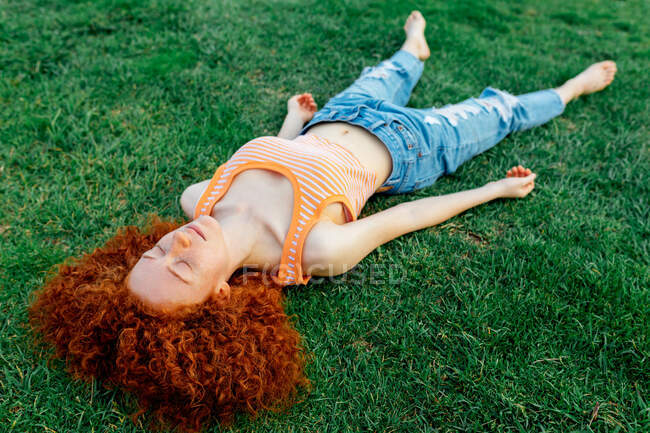 Alto ângulo de corpo inteiro de mulher ruiva serena com olhos fechados descansando na grama na natureza — Fotografia de Stock