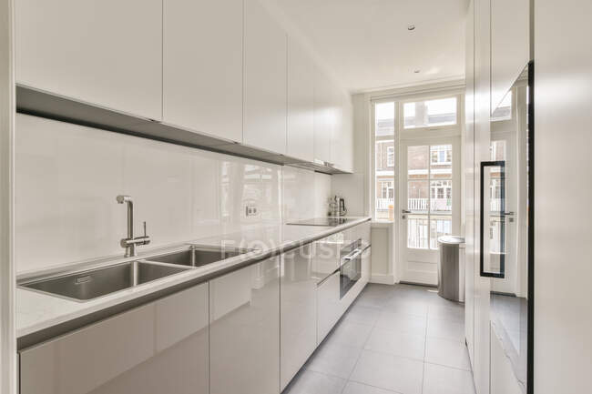 Enge sonnendurchflutete Küche mit minimalistischen weißen Möbeln und Balkontür in zeitgenössischer Wohnung — Stockfoto