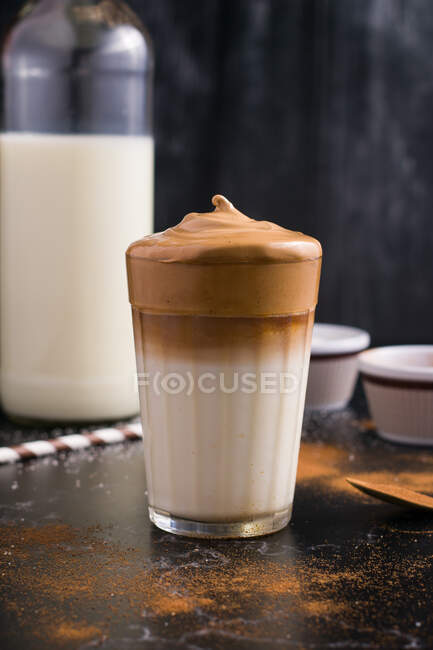 Стакан вкусного кофе Далгона с молоком и пенной начинкой помещен на черный грязный стол с какао-порошком и сахаром — стоковое фото