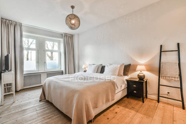 Кровать с покрывалом и подушками под лямкой висит у окна дома с деревянным полом — стоковое фото