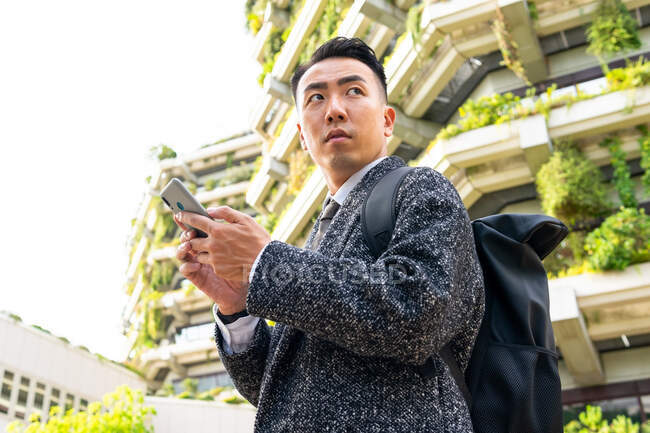 Снизу молодой этнический предприниматель с галстуком смотрит в сторону, разговаривая по сотовому телефону в городе — стоковое фото