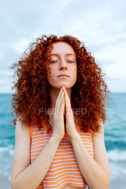 Donna pacifica in piedi con gli occhi chiusi sulla riva del mare e fare gesto namaste durante la meditazione — Foto stock
