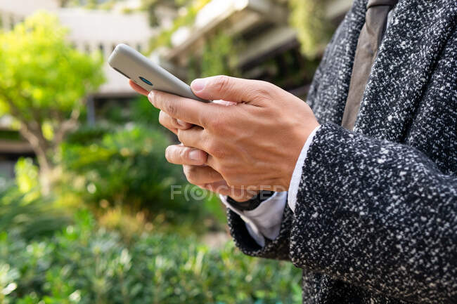 Обрезанный неузнаваемый мужчина-предприниматель с галстуком смотрит в сторону, разговаривая по мобильному телефону в городе — стоковое фото