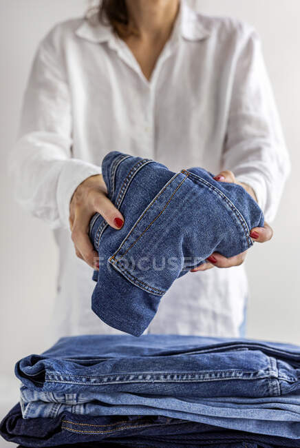 Cortar fêmea anônima em camisa branca com pilha de jeans azuis nas mãos — Fotografia de Stock
