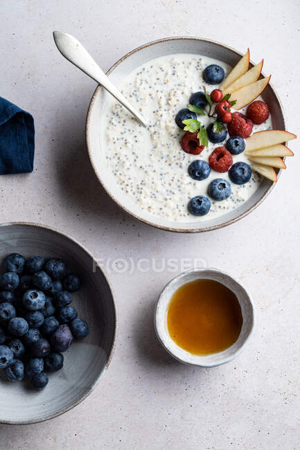 Чаша с вкусной кашей, увенчанная черникой и малиной возле ломтиков груши, подаваемых на стол во время завтрака — стоковое фото
