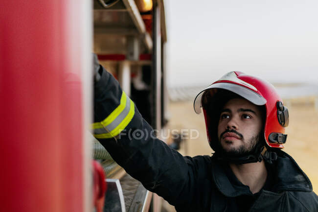 Operaio tranquillo con uniforme protettiva e cappello rosso che opera all'interno di camion dei pompieri — Foto stock