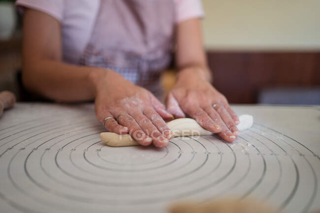 Ernte gesichtslose Frau in Schürze Teig rollen mit den Händen auf dem Tisch, während die Zubereitung hausgemachter Knödel in der Küche — Stockfoto