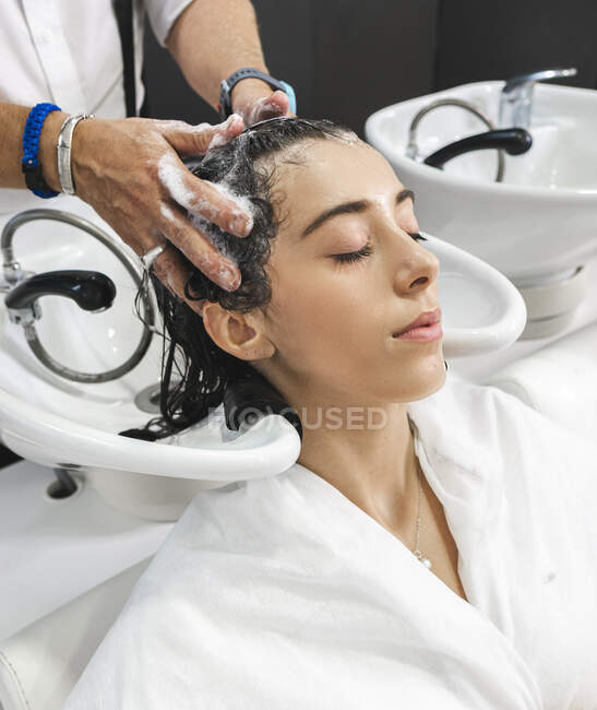 Врожай невідомий майстер миття темного волосся жіночого клієнта із закритими очима в салоні краси — стокове фото