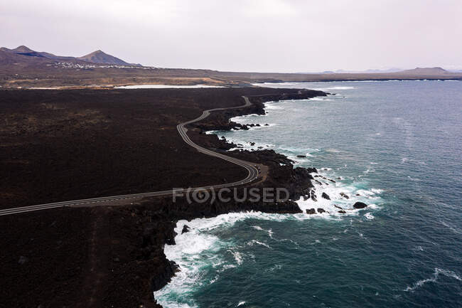 Вид на пенное море с беспилотника на извилистую дорогу и горы с Hervideros в Yaiza Lanzarote Канарские острова Испания — стоковое фото