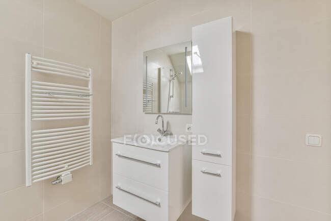 Creative design of bathroom with heated towel rail against washstand with tap under mirror in light house — Stock Photo