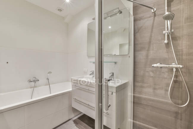 Шафа з раковиною та дзеркалом, розташована між ванною та скляною душовою кабіною у світлій сучасній ванній кімнаті — стокове фото