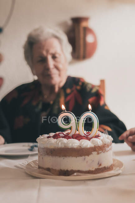 Ältere Frau bläst Kerzen auf Geburtstagstorte und klatscht dann in die Hände, während sie mit Verwandten zu Hause ihren 90. Geburtstag feiert — Stockfoto
