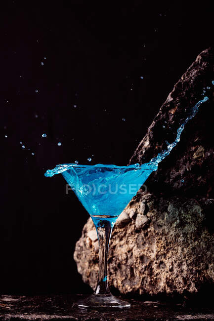 Коктейль Blue Lagoon из хрустального элегантного стекла, размещенного на грубой поверхности на черном фоне — стоковое фото