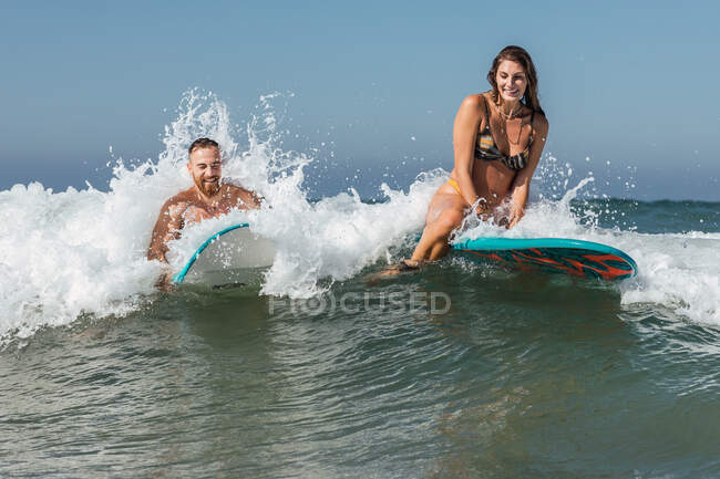 Deportistas en traje de baño en tablas de surf surfeando en el mar con olas espumosas en el resort tropical en el soleado día de verano - foto de stock