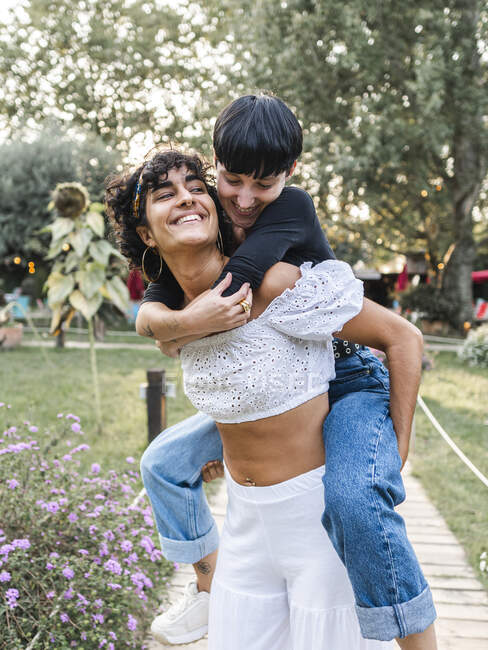 Lächelnde Frau huckepack erfreut Freundin beim Spaß am Wochenende im Sommerpark — Stockfoto