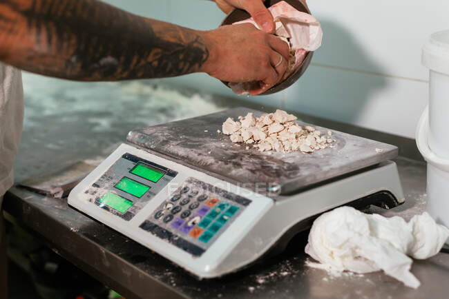 Cultivo irreconhecível tatuado chef masculino pesando pedaços de fermento fresco em balanças eletrônicas durante o pão de cozimento na cozinha — Fotografia de Stock