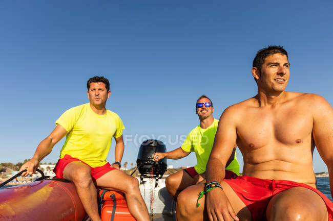 Lifeguards sitting on inflatable motorboat floating on rippling blue sea and controlling safety on sea — Stock Photo