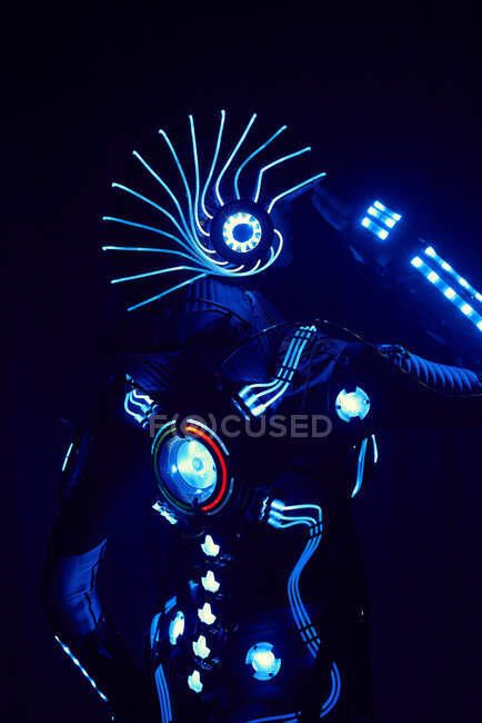 Безликий человек в костюме ведущего космического киборга со шлемом и светящейся неоновой подсветкой стоит на черном фоне в студии — стоковое фото