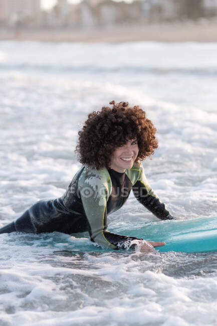 Side view of young happy female surfer in wetsuit lying on waving seawater and enjoying summer day — Stock Photo