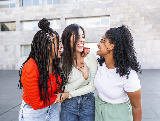 Fröhliche, multiethnische Frauen, die bei Tageslicht zusammen auf der Straße stehen und lachen — Stockfoto