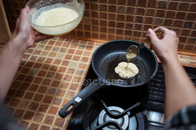 Зверху урожаю анонімні жінки готують смачні млинці на сковороді на плиті на кухні — стокове фото