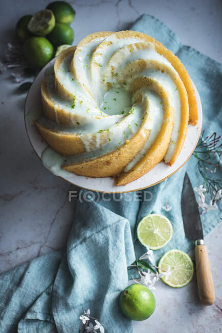 Top view of tasty lime sponge cake served on white plate near flowers and lime slices — Stock Photo