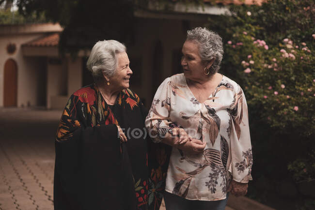 Старі жінки носять повсякденний одяг і розмовляють під час прогулянки в літньому саду біля зелених кущів троянд в похмурий день — стокове фото