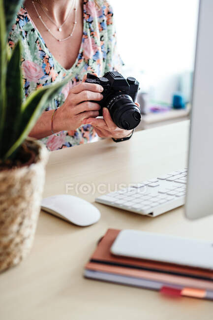 Side view of anonymous female photographer with professional camera in blurred room against computer — Stock Photo