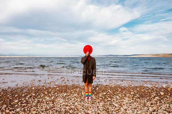Unbekannter mit rotem Hut und Mantel steht im Sommer in Ufernähe mit Schotter — Stockfoto