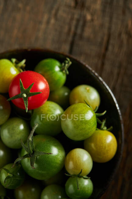 De dessus de tomates cerises vertes et rouges entières dans un bol recueilli à la ferme pendant la saison des récoltes — Photo de stock