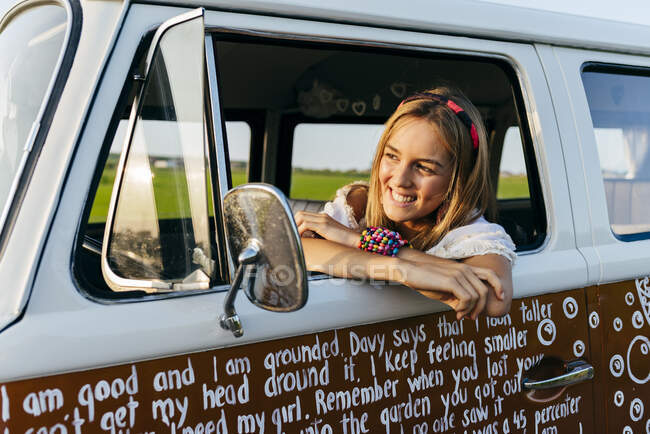 Симпатична блондинка сидить всередині старовинного фургона і спирається на вікно в сонячний день — стокове фото