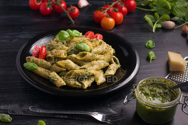 Сверху тарелки подают вкусную пасту с зеленым соусом песто и помидорами на черном деревянном столе — стоковое фото