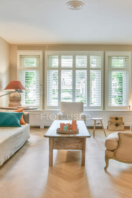 Modernes Wohnzimmerinterieur mit Kerzen auf dem Tisch zwischen Sofa und Sesseln gegen Fenster mit Jalousien zu Hause — Stockfoto
