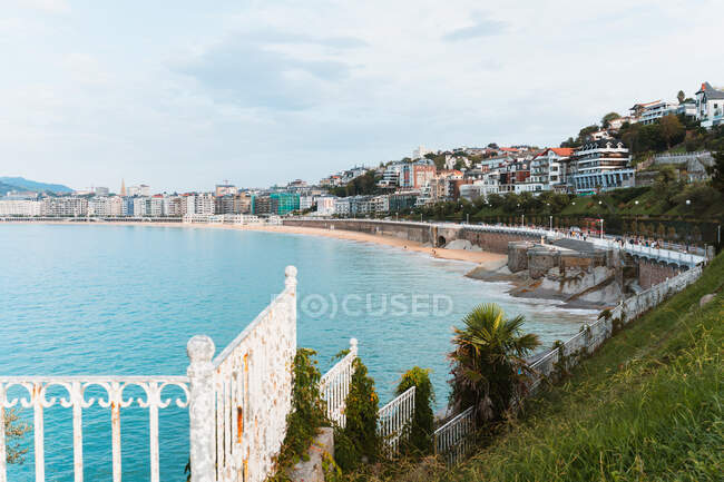 Picturesque scenery of calm blue water of Bay of Biscay washing embankment with walkway and residential buildings in San Sebastian in Spain under cloudy blue sky in daylight — Stock Photo