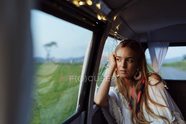 Впевнена красива блондинка, що спирається на вікно всередині вінтажного фургона, дивлячись далеко — стокове фото
