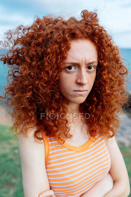 Расстроенная женщина с вьющимися рыжими волосами, проявляющая эмоции недовольства и смотрящая в камеру — стоковое фото