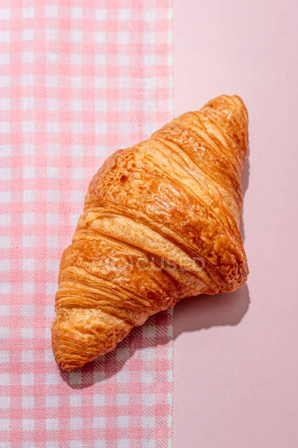 De cima de delicioso croissant doce colocado na toalha de mesa rosa na mesa à luz do dia — Fotografia de Stock