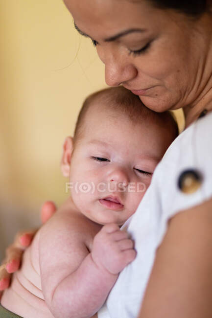 Боковой вид на урожай спокойная молодая женщина обнимает и ласкает очаровательного ребенка в дневное время — стоковое фото