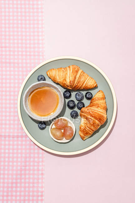 Vue de dessus de délicieux croissants servis sur une assiette en céramique avec des bleuets frais et de la confiture placée sur une table rose — Photo de stock