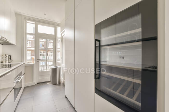 Armoire simple avec portes blanches et vitrées située dans une cuisine étroite dans un appartement moderne — Photo de stock