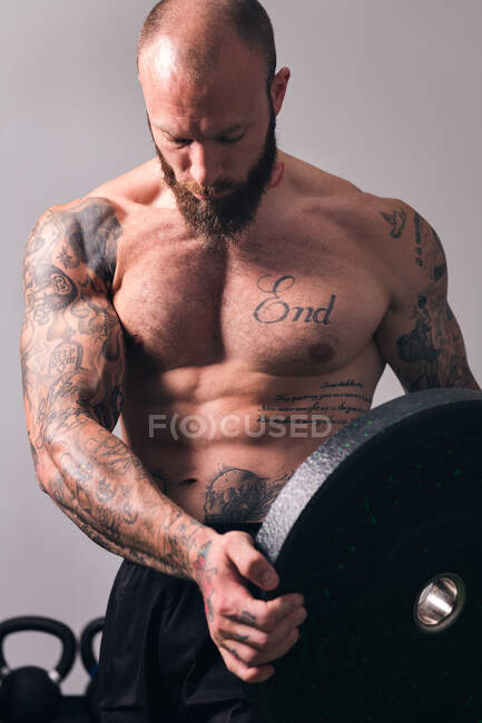 Sportler mit muskulösem Körper und nacktem Oberkörper steht mit schwerer Hantelscheibe im Fitnessstudio — Stockfoto