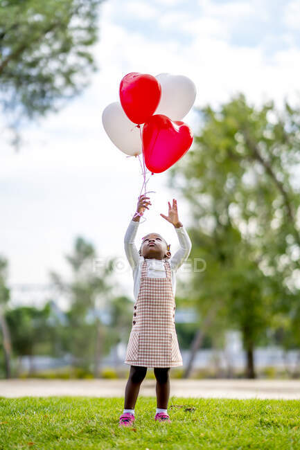 Allegro ragazza afroamericana con trecce in abiti eleganti in esecuzione con palloncini colorati in mano nel parco durante il giorno — Foto stock
