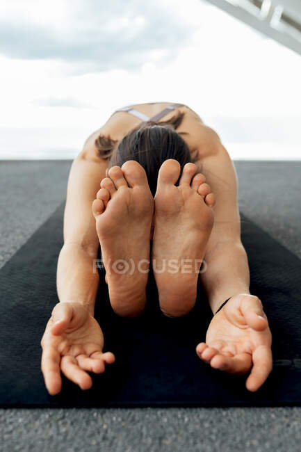 Unrecognizable flexible barefoot female practicing Paschimottanasana posture on mar during yoga training near solar panel on street in Barcelona city — Stock Photo